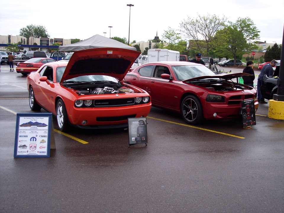 Orange Dodge Challenger and red Dodge Charger parked side-by-side with hoods open