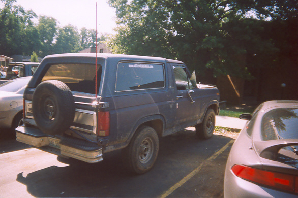 Dark blue 1980s Ford Bronco with spare tire on rear door, parked in a lot