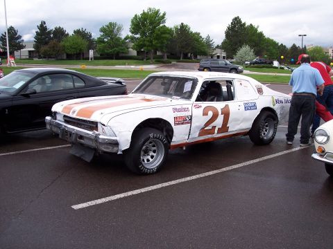 1972 Ford Ranchero - A white race car with orange stripes and the number 21 is parked in a lot next to a black car.