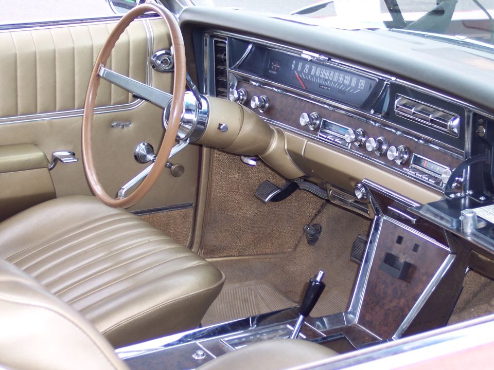 Car interior with tan seats, wood grain dash, and steering wheel. Speedometer and radio visible