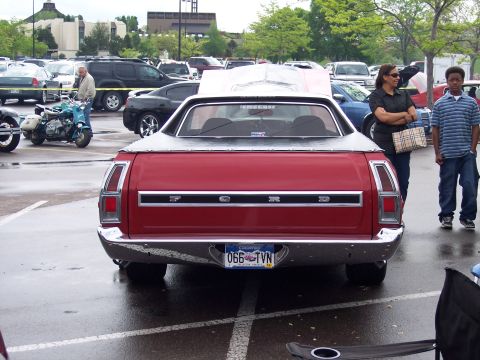 1972 Ford Ranchero - A red Ford Ranchero pickup truck is parked in a lot with other vehicles and people around.