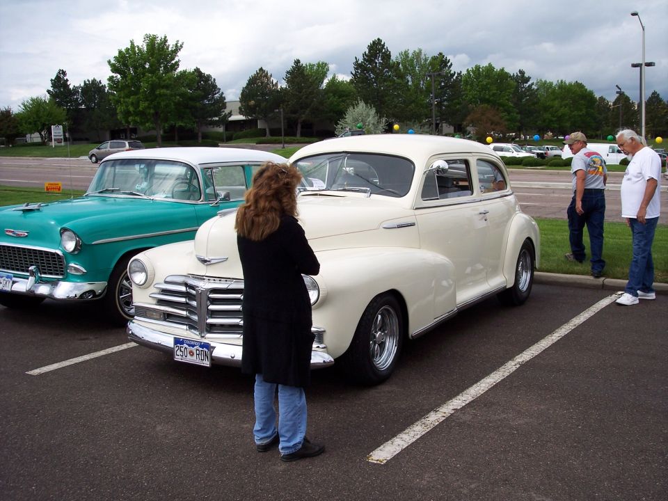 cream colored sedan parked next to a teal car, people looking at cars