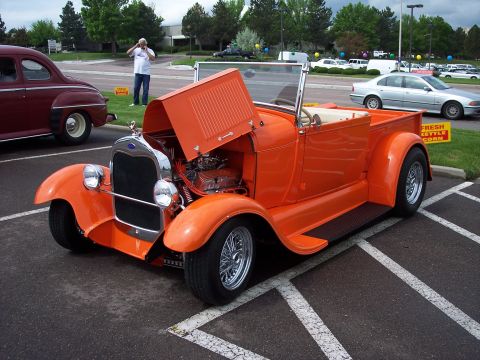 1972 Ford Ranchero - Orange 1928 Ford hot rod pickup truck, hood open, parked in a lot with other vehicles.