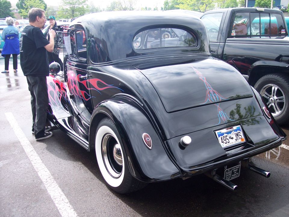 Black hot rod coupe with red and pink flames on the side and pinstriping on the trunk, parked next to a black pickup truck