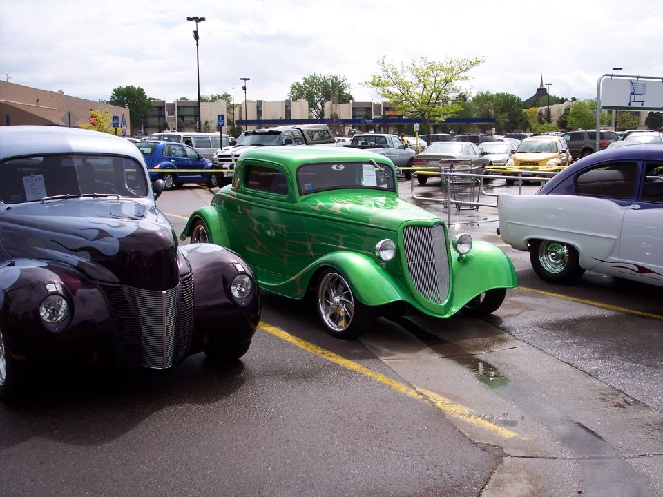 Green 1934 Ford hot rod coupe parked next to a purple hot rod and a two-tone sedan