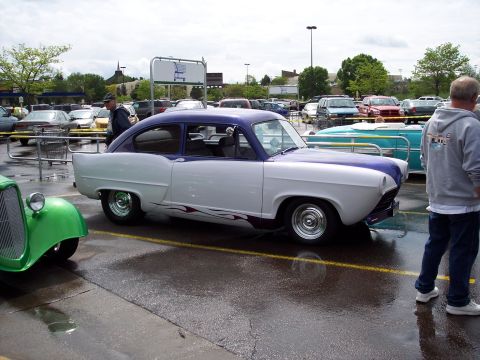 1972 Ford Ranchero - A two-tone sedan with flame decals is parked in a wet parking lot next to a green hot rod.