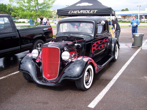 1972 Ford Ranchero - A black hot rod with red flames and whitewall tires is parked next to a pickup truck under a Chevrolet tent.