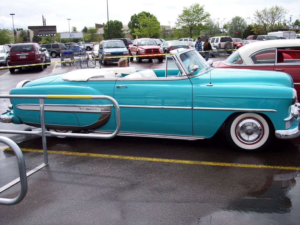 Turquoise convertible with white top and whitewall tires parked in a wet parking lot