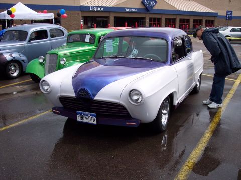 1972 Ford Ranchero - A man examines a custom white and purple coupe parked in a lot with other classic cars. The license plate is visible.