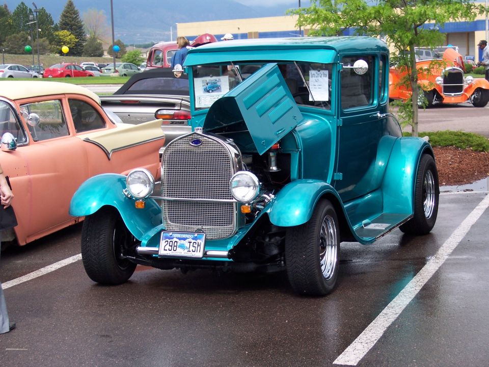 Teal 1929 Ford Model A coupe hot rod with hood open, parked next to a pink and cream car