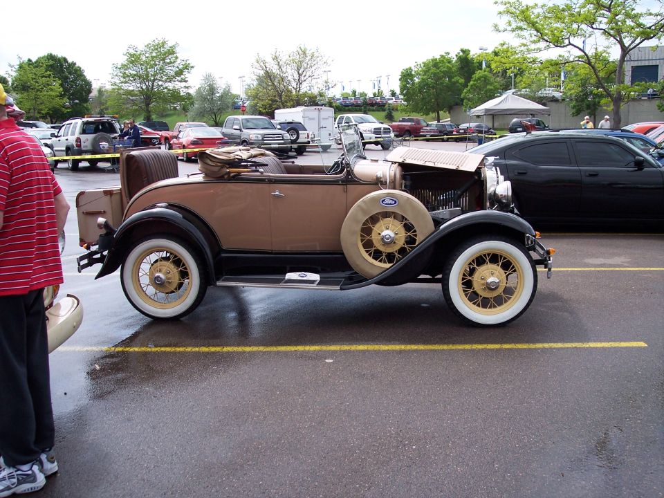 Tan antique convertible with a spare tire on the side, parked in a lot