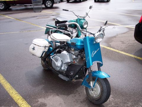 1972 Ford Ranchero - Two scooters are parked in a lot, one blue and one green, with yellow lines on the ground.