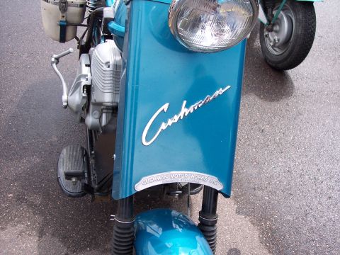 1972 Ford Ranchero - Front view of a blue Cushman scooter, the "Cushman" script and "Cushman Motor Works Inc." badge. Another vehicle is partially visible in th…