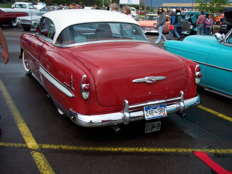 Rear view of a red and white 1954 Chevrolet Bel Air parked on a wet asphalt lot