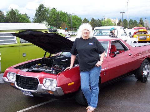 1972 Ford Ranchero - A woman stands by a red 1972 Ford Ranchero at an outdoor event with other vehicles present.