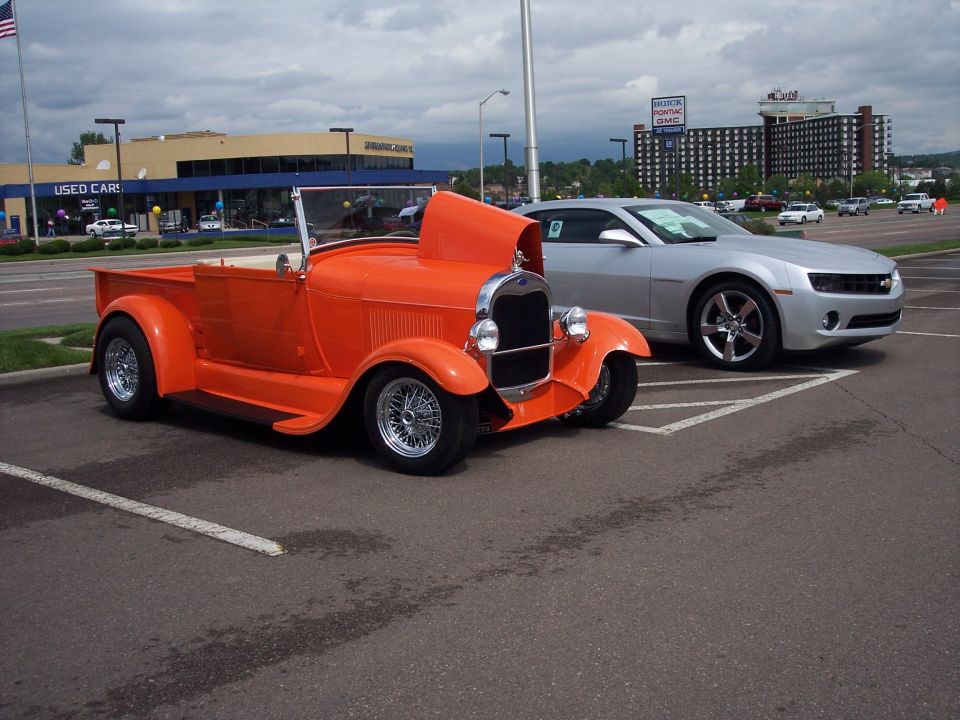 Orange hot rod pickup truck parked next to a silver Chevrolet Camaro
