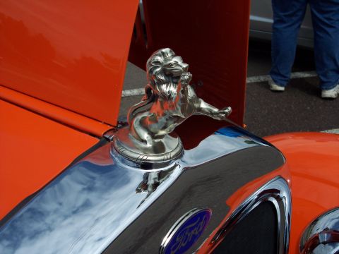 1972 Ford Ranchero - A chrome lion hood ornament sits atop the grille of an orange vehicle, reflecting the sky.