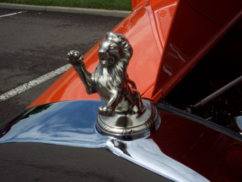 1972 Ford Ranchero - A detailed chrome lion hood ornament adorns the front of a vintage car, its striking orange and dark red paint scheme.