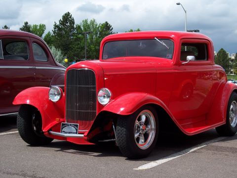 1972 Ford Ranchero - A red 1932 Ford hot rod coupe is parked next to another vehicle under a cloudy sky.