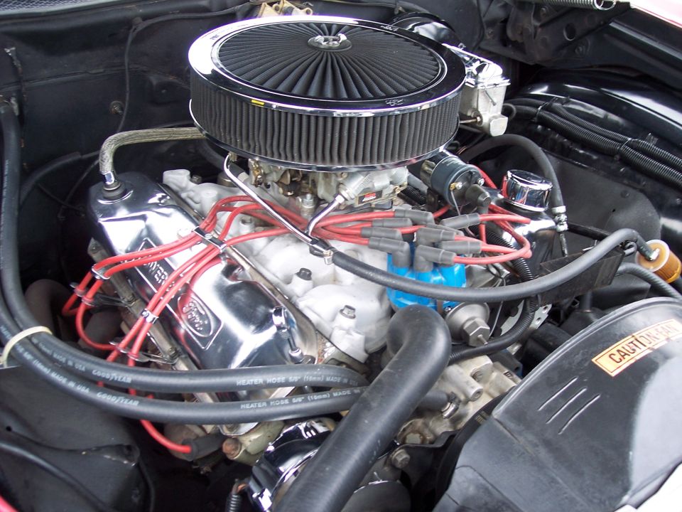 Close-up of a Ford V8 engine with chrome valve covers and a large air filter. Red spark plug wires are visible