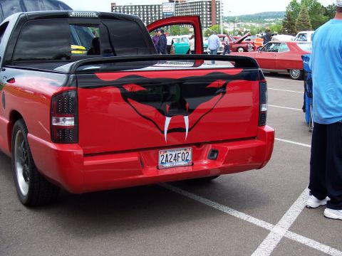 1972 Ford Ranchero - A red pickup truck with a custom snake graphic on the tailgate is parked in a lot with other vehicles.