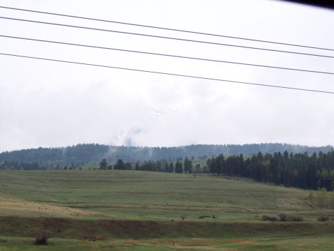1972 Ford Ranchero - A wide landscape shot captures rolling green hills and a distant forest under a cloudy sky, with power lines overhead.