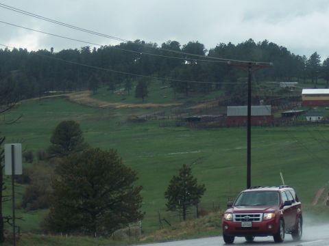 1972 Ford Ranchero - Red SUV drives on a wet road past a rural farm scene under an overcast sky.