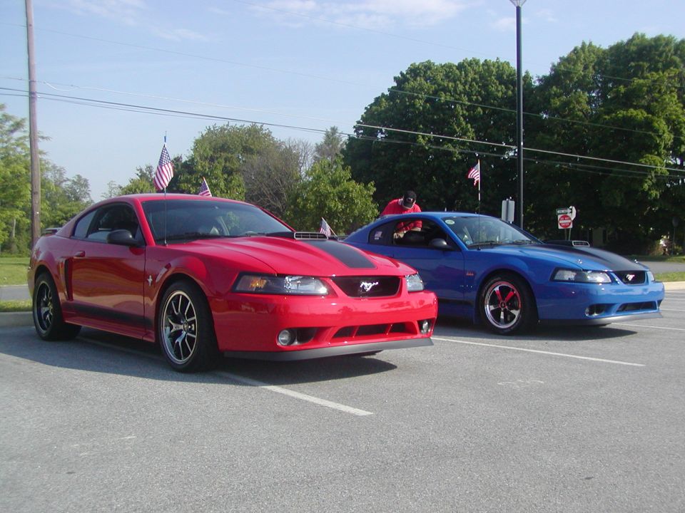 Red 2004 Ford Mustang parked next to a blue one, both with racing stripes