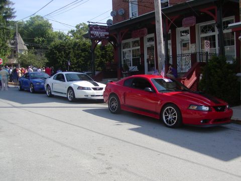 2004 Ford Mustang - Several Ford Mustangs are lined up on a street, with a restaurant in the background.