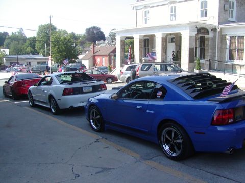 2004 Ford Mustang - Multiple Ford Mustangs parked in front of a building with American flags displayed.