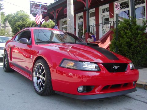 2004 Ford Mustang - Red 2004 Ford Mustang with black racing stripes parked in front of a building.