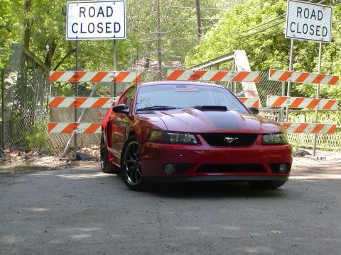 2004 Ford Mustang - A red Ford Mustang is stopped at a road closure, indicated by signs and barricades.