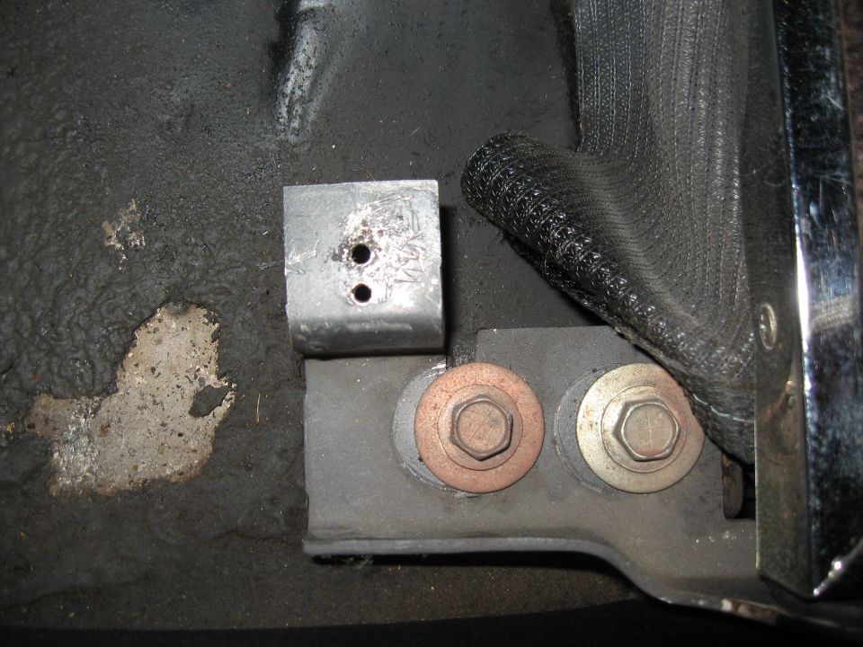 Close-up of a seatbelt anchor bracket with two bolts and a metal plate