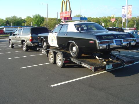 2001 Ford Crown Victoria - A 1975 Dodge Monaco police car is transported on a trailer, with a Chevrolet Suburban in the background.