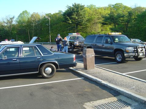 2001 Ford Crown Victoria - Several police vehicles, including a dark blue 2001 Ford Crown Victoria, are parked in a lot under a clear sky.