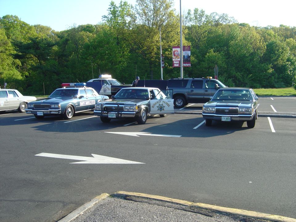Four police cars and an SUV parked in a lot. One car has its door open
