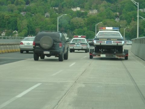 2001 Ford Crown Victoria - A police car is being towed on a trailer, with other vehicles on the road.
