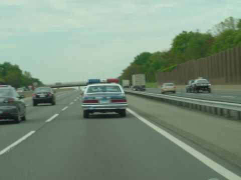 2001 Ford Crown Victoria - A police car with a light bar is seen from behind on a multi-lane highway, with other vehicles in traffic.