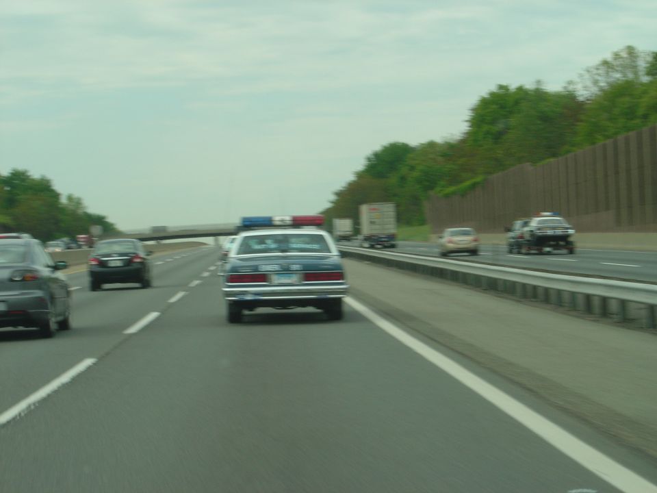 Police car with light bar driving on highway, other cars and trucks also visible