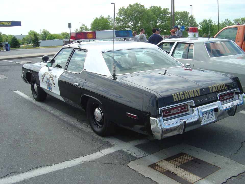 Rear view of a black and white Dodge highway patrol car with chrome bumper and license plate V-37254