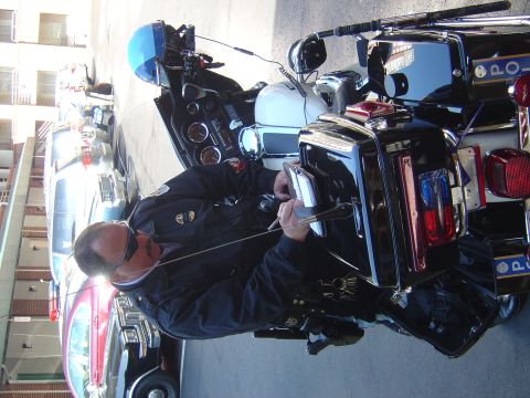 2001 Ford Crown Victoria - Officer on a police motorcycle, writing a ticket next to a silver car.