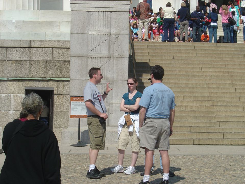 Tourists gather on wide stone steps in front of a large building with people in the background