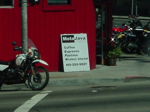 1979 Ford Bronco - A white motorcycle is parked on the street in front of a red building with a sign for MotoJava.