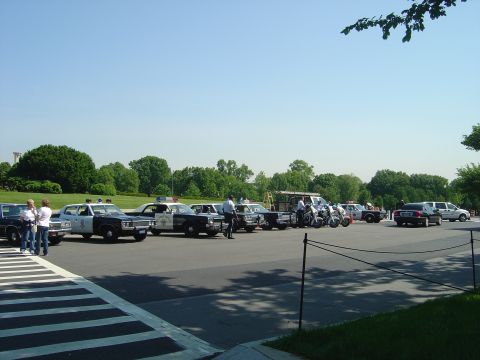 2001 Ford Crown Victoria - A line of police vehicles, including cars and motorcycles, are parked outdoors on a sunny day.