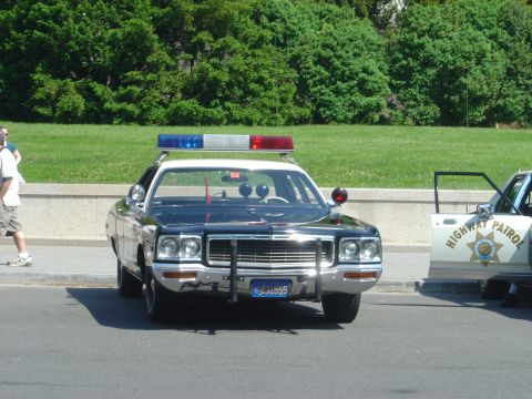 2001 Ford Crown Victoria - A vintage police car with a light bar is parked on the street next to another highway patrol vehicle.
