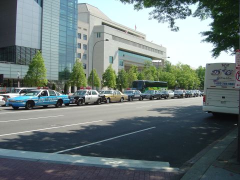 2001 Ford Crown Victoria - A row of police vehicles and a bus are parked along a street in front of modern buildings.