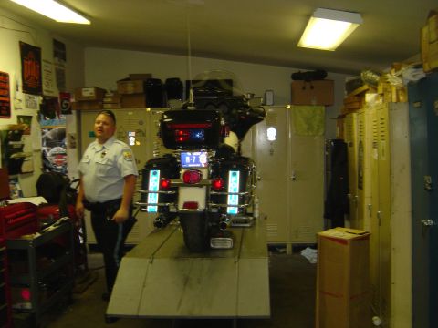 2001 Ford Crown Victoria - A police officer stands next to a motorcycle on a ramp inside a garage.