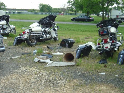 2001 Ford Crown Victoria - Disassembled police motorcycles and scattered parts lie on the ground next to a road, possibly damaged, police motorcycle.