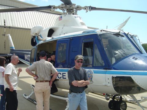 2001 Ford Crown Victoria - A blue and white police helicopter is parked on the tarmac with several people standing nearby.