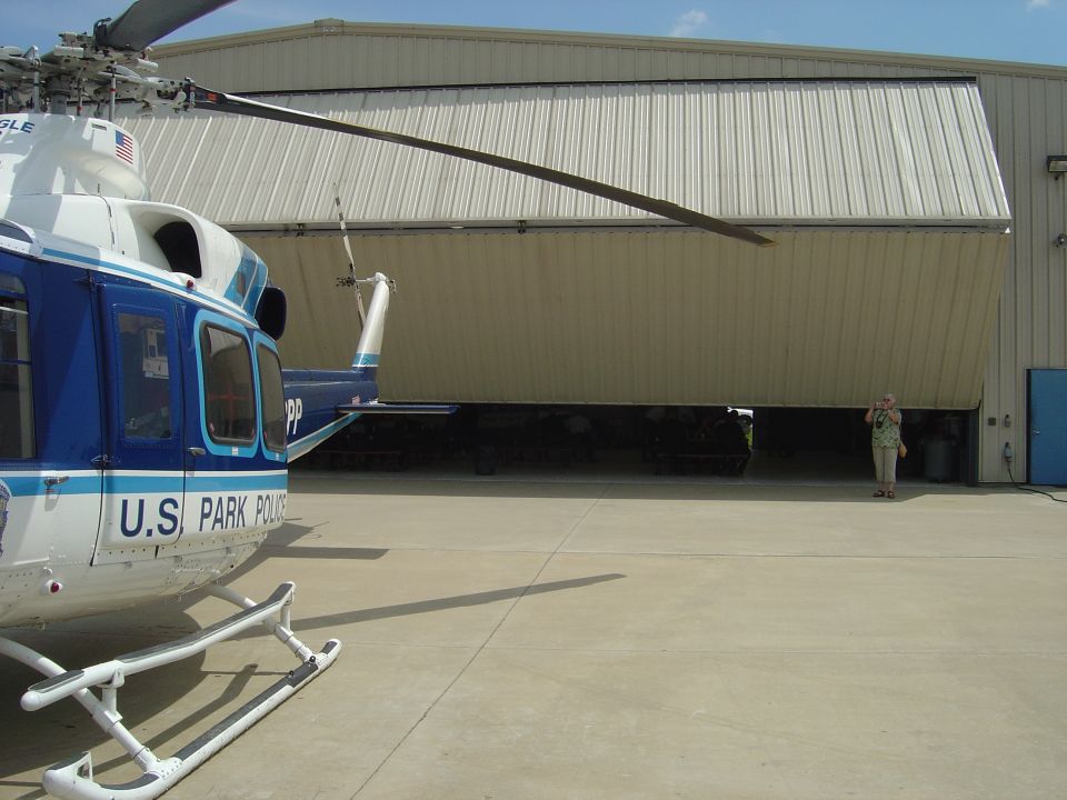 U.S. Park Police helicopter parked on tarmac in front of open hangar with another helicopter inside